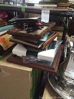 Stack of various framed wall art pieces and empty frames piled on a cardboard box.