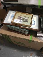 Stack of framed art prints on top of a cardboard box with visible box labels.