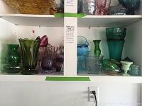 Shelf with multiple colored glass items including green vases, purple glass pieces, and a milk glass vase.