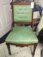Front view of upholstered wooden chair with floral patterned green fabric on seat and backrest, showcasing carved wood frame and casters on front legs.