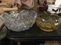 Two bowls on black surface: large clear crystal bowl with complex cut pattern and amber glass bowl
