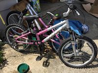Side view showing pink and silver frame, multiple speed gears, coiled rear shock absorber, front suspension fork, knobby tires, and pedals.
