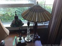 Photo showing three lamps on a wooden surface near window: the larger Tiffany reproduction lamp with stained glass shade, smaller Tiffany reproduction desk lamp with stained glass shade and adjustable arm, and the glass ball-base lamp without shade.