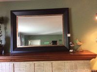 Mirror mounted on a mantel showing the full front of the mirror reflecting a room.