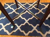View of Safavieh Cambridge rug under table legs, showing blue background and cream lattice pattern.