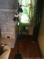 Black metal pole lamp with two vented adjustable lights beside a stone wall and window