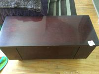 Top down view of the rectangular wooden blanket chest showing dark wood surface with clear signs of water damage and surface scratches.