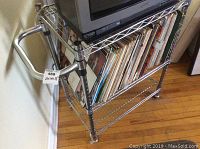 Side view of chrome metal cart showing wire mesh shelves, handle, and some contents (excluded).