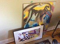 Two pieces of wall art leaning against a wall, showing the original oil painting and the larger poster board print.