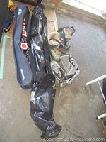 Head skis, ski poles, snow blades in black bags, two pairs of boots including skis and skates arranged on floor.