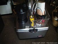 Full lot with Coleman cooler as base, bug zapper on top left, metal basket on top right containing various small items including extension cords and papers.