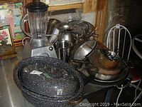 Photo of the lot including the speckled roasting pan, metal sifters, electric blender, several frying pans, mixing bowls, and metal utensils on a table.