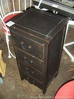 Front angled view of the black wooden cabinet with visible wear and metal drawer handles.