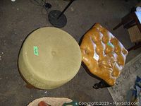 Photo showing a round wooden and cloth covered foot stool alongside a square leather tufted foot stool.