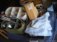Two metal caddies filled with various kitchen utensils and knives, placed on a chair with a cloth covering part of the items.