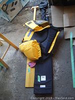 Wooden oar laying on the ground with yellow Salus life jacket folded on top, black soft storage case underneath