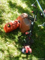 Toro gas trimmer lying on grass with two red gas cans adjacent showing overall outdoor wear and untested condition.