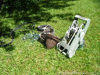 Full lot outdoor photo showing the hose caddy upright, wicker baskets, and garden hose on green grass.