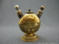 Front view of the vintage brass table lighter showing embossed floral and heart patterns and two spherical capped lighting mechanisms on top.