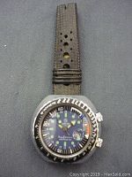 Top-down view of vintage Mortima men's watch showing black dial with luminous markers, tachymeter bezel, and worn perforated black leather strap.