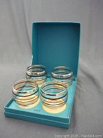 Four hand-blown glasses placed inside a blue Birks box, showing the glasses inside the box with visible silver stripes.
