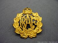 Front view of WWII-era RCAF cap badge showing crown, RCAF letters, and laurel wreath in gold-tone metal.