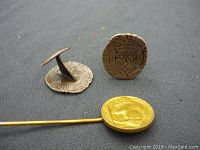 Two silver-colored vintage coin cuff links and one gold-colored coin stick pin on grey fabric.