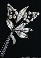 Front view of large sterling silver floral spray brooch showing multiple flowers and leaves with hammered texture on black background.