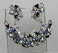 Front view of crescent moon shaped brooch displaying opalescent plum, blue, and rhinestone glass stones in settings.