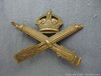 Front view of the WWI Canadian Machine Gun Corps brass cap badge showing detailed crossed machine guns and crown design.