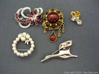 Five pieces of vintage costume jewellery displayed on grey cloth background.