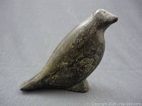 Front and side view of dark soapstone carved bird figure on dark fabric background.