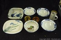 Overview of nine pottery pieces including plates, bowls, cups with floral and bird designs on dark background.