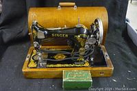Vintage Singer sewing machine with original wooden coffin case in background. Machine decorated with gold and red floral decals on black metal body.
