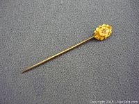 Front angle view of the small Victorian stick pin showing the gold floral top with gemstone and the slender twisted shaft.