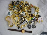 Large heap of assorted vintage costume jewelry items including earrings, brooches, and a wristwatch laid on a white cloth.