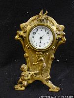 Frontal view of clock showing the gold-tone Art Nouveau style bezel with cherub and bird decoration around the round clock face with Arabic numerals.