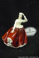 Full view of Royal Doulton figurine "Gail" in red skirt and white blouse holding a white hat.