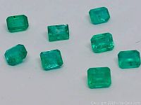Photo showing 8 natural emeralds laid out loosely on a flat surface, displaying their rectangular step cut and vibrant green color.
