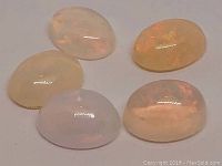 Five oval cabochon cut Ethiopian opals arranged on plain light background, showing varying translucent base colors and opal flash.