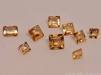 Photo of 9 natural Brazilian citrine gemstones with various square and rectangular modified cuts on a neutral background.
