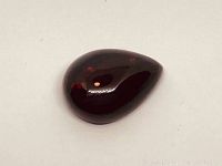 Top view of pear-shaped cabochon black opal showing dark body with red flashes.
