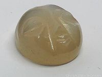 Oval carved moonstone moon face gemstone showing carved details and translucent pale yellow color.
