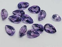 Close-up of 13 pear cut purple amethyst gemstones spread out showing facets and color