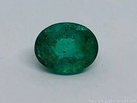 Oval green Columbian emerald gemstone, top-down view showing polish and facet detail along with inclusions.