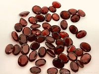 Top view photo showing the 56 faceted deep red Pyrope garnets, mostly oval, scattered on a white background.