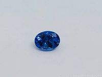 Close-up photo of oval deep purple tanzanite gemstone, showing faceted surface and color.