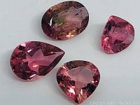 Four natural pink tourmaline gemstones on white background, showing faceted cuts and varying pink colors including one oval and three pear shapes.