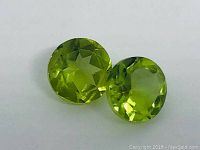 Front view of matched pair of round diamond cut peridot gemstones showing bright yellow-green color and internal facets.