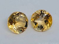 Front photo of the matching pair of round golden yellow diamond cut citrine stones showing facets.
